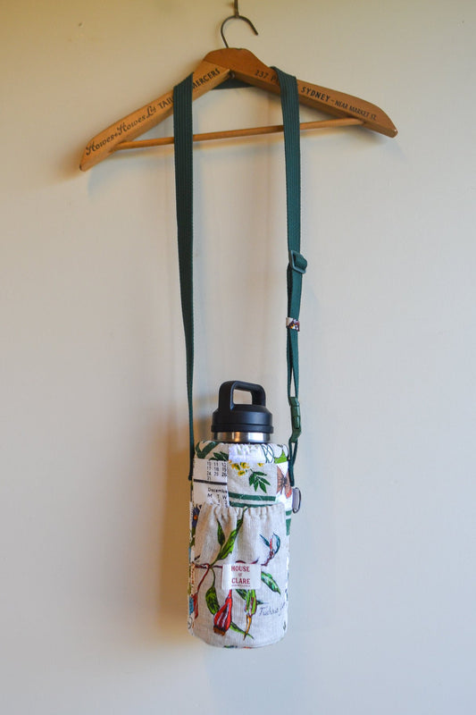 Floral-patterned water bottle holder with a black lid on a hanger against a white wall